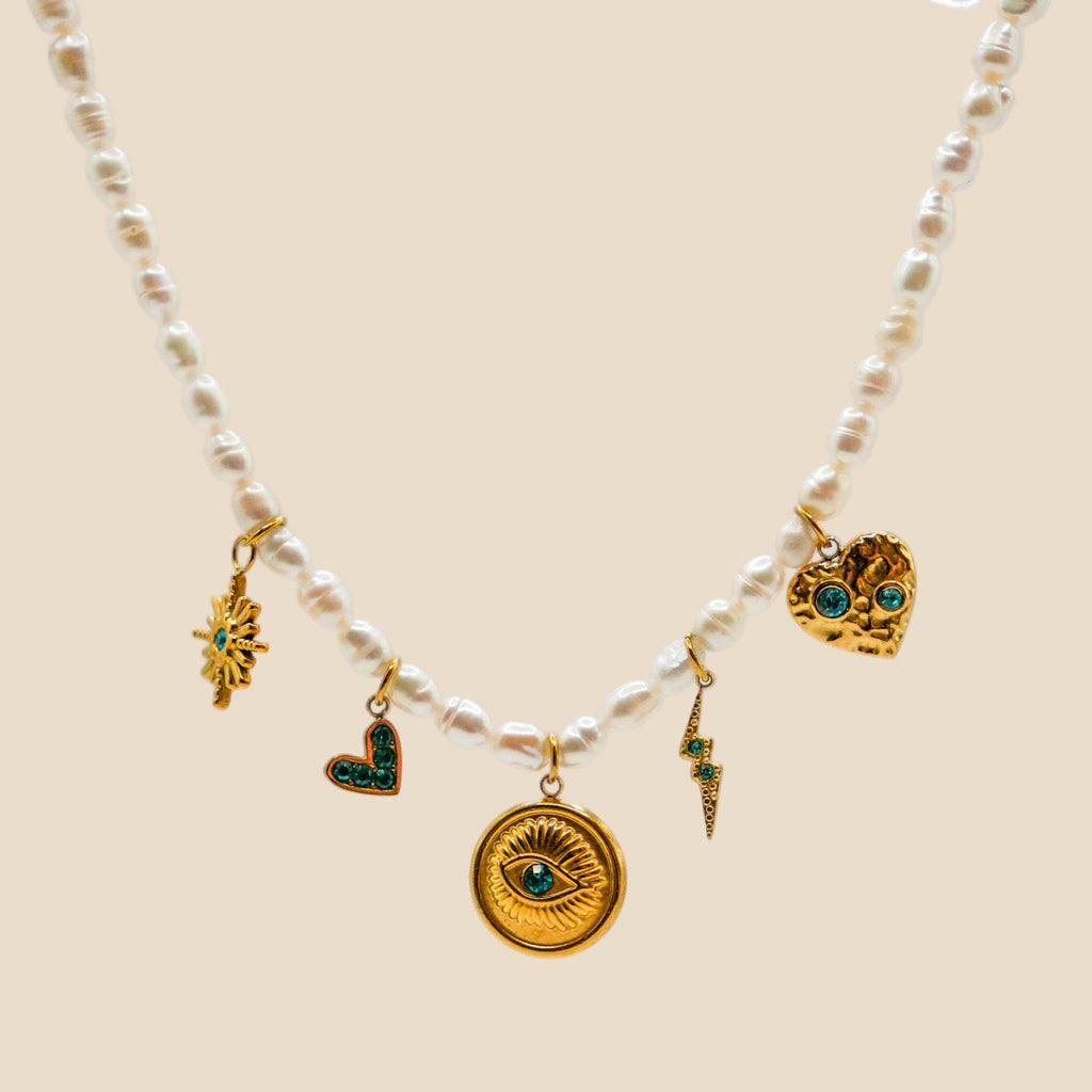Freshwater pearl necklace with 18K gold-plated stainless steel charms featuring an eye medallion, green crystal hearts, lightning bolt, and star motif.