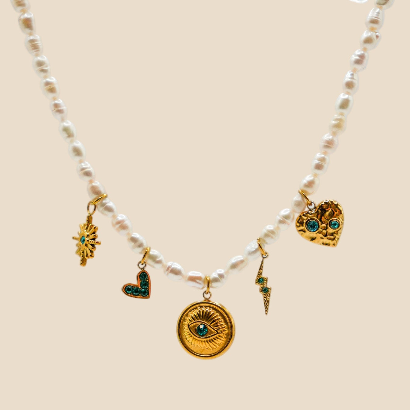 Freshwater pearl necklace with 18K gold-plated stainless steel charms featuring an eye medallion, green crystal hearts, lightning bolt, and star motif.